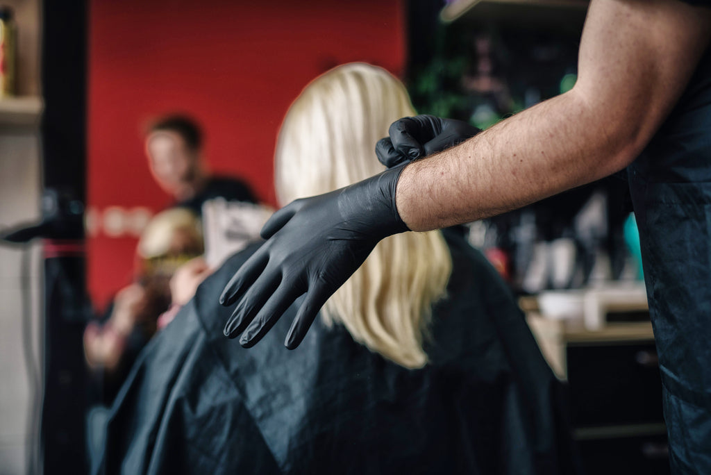 Hair stylist snaps on a black Raxwell glove before coloring a client’s hair. Photo showcases salon hygiene and tactile control.