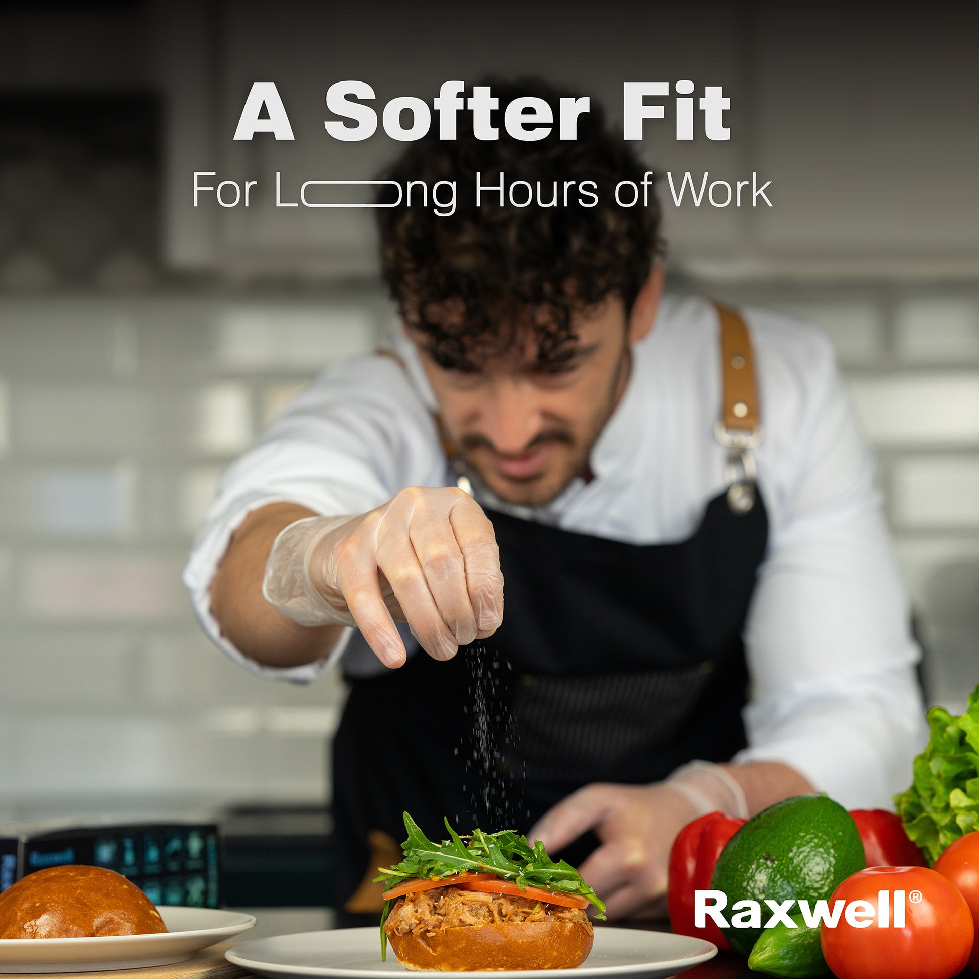 Chef in apron seasons a sandwich while wearing clear Raxwell vinyl gloves beneath the text “A Softer Fit for Long Hours of Work.” The image highlights comfort and flexibility in professional kitchens.